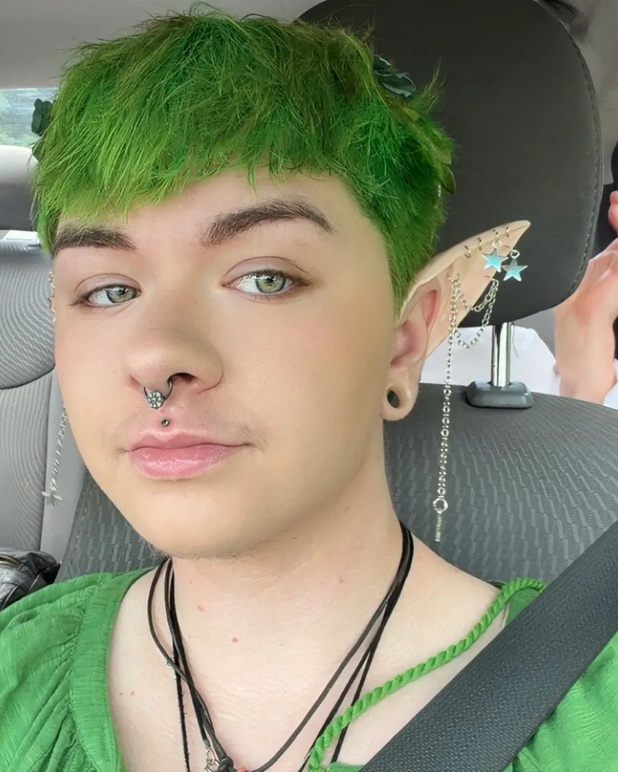 Asher Rivera, owner and hairstylist, with green hair, fae ear cuffs and star earrings